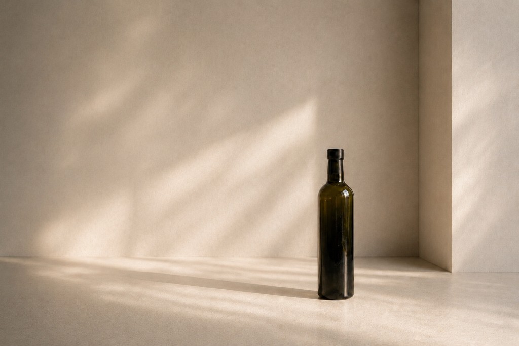 An unlabeled dark green glass bottle in a sunlit corner, standing in for a physical product whose identity is still invisible